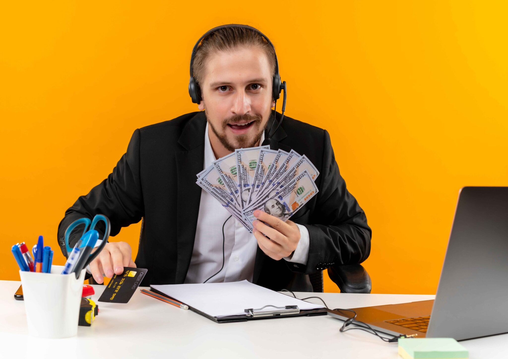 handsome-businessman-suit-headphones-with-microphone-showing-cush-looking-camera-happy-excited-sitting-table-office-orange-background