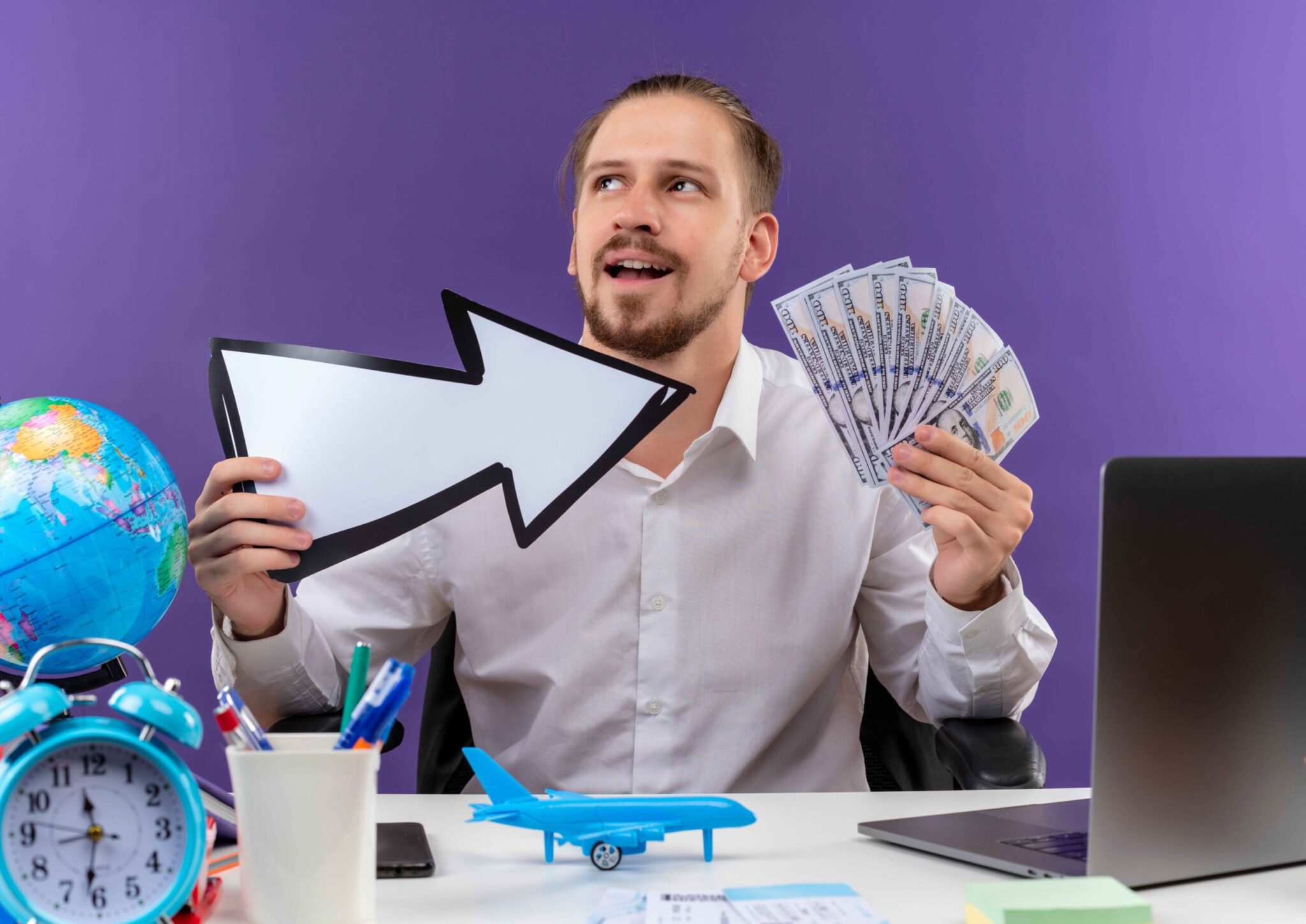 handsome-businessman-white-shirt-holding-white-arrow-showing-cash-looking-aside-with-smile-face-sitting-table-offise-purple-background